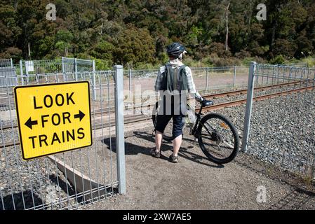 Ciclista donna che attraversa attentamente la linea ferroviaria vicino a Ohakune, Isola del Nord, nuova Zelanda. Foto Stock