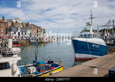 Porto di Weymouth con barche da pesca ormeggiate e turisti che cenano sul fronte del porto di Weymouth, Dorset, Regno Unito il 16 agosto 2024 Foto Stock