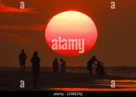 Isola di Palms, Stati Uniti. 18 agosto 2024. Gli amanti della spiaggia, che si stagliano dall'alba, osservano il sole che esce dall'orizzonte in un'altra giornata calda e umida sulla spiaggia di Wild Dunes, 18 agosto 2024, a Isle of Palms, South Carolina. I giorni continuano negli anni novanta e le temperature oceaniche superano i 83 gradi. Crediti: Richard Ellis/Richard Ellis/Alamy Live News Foto Stock