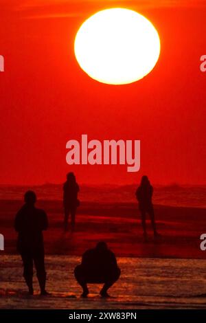 Isola di Palms, Stati Uniti. 18 agosto 2024. Gli amanti della spiaggia, che si stagliano dall'alba, osservano il sole che esce dall'orizzonte in un'altra giornata calda e umida sulla spiaggia di Wild Dunes, 18 agosto 2024, a Isle of Palms, South Carolina. I giorni continuano negli anni novanta e le temperature oceaniche superano i 83 gradi. Crediti: Richard Ellis/Richard Ellis/Alamy Live News Foto Stock