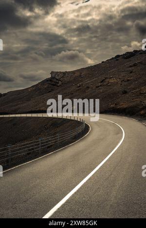 Una strada tortuosa attraversa l'aspro paesaggio vulcanico dell'Islanda sotto un cielo spettacolare Foto Stock