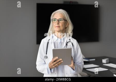 Terapeuta di mezza età che tiene in mano il tablet guardando a distanza Foto Stock