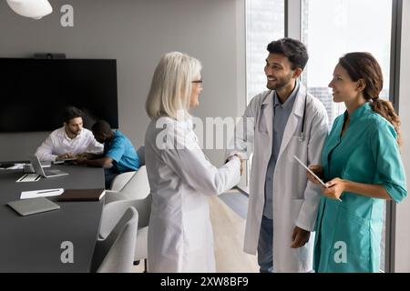 Medico donna esperto che stringe la mano con un medico maschio più giovane Foto Stock