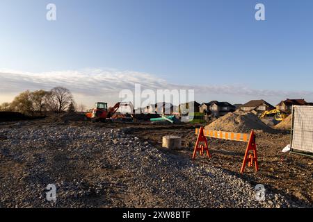 Cantiere illuminato al tramonto con escavatore rosso e materiali da costruzione sparsi - sfondo del quartiere periferico. Presa a Toronto, Canada. Foto Stock