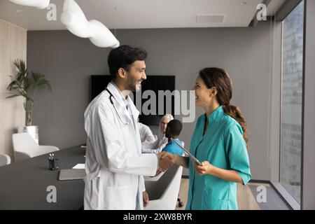 Due giovani professionisti del settore sanitario stringono la mano mentre si trovano in sala riunioni Foto Stock