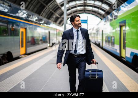 Un uomo d'affari in costume attraversa la trafficata stazione ferroviaria con le valigie, pronto per un viaggio di lavoro. L'ambiente urbano aggiunge un tocco moderno. Sorridendo, lui lo Foto Stock