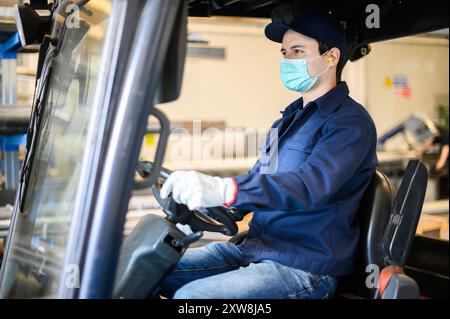 Un bel lavoratore di costruzione che guida un carrello elevatore in un impianto industriale Foto Stock