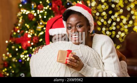 Felice donna afro abbracciando il suo fidanzato e azienda confezione regalo Foto Stock