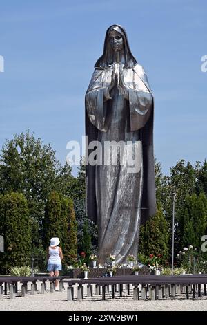 Grande statua in acciaio inossidabile della Vergine Maria al Santuario Vodica-Mariakert di Hercegszántó con donna solitaria che prega in estate da un angolo Foto Stock