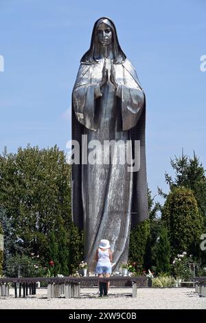 Grande statua in acciaio inossidabile della Vergine Maria al Santuario Vodica-Mariakert di Hercegszántó con donna solitaria che prega in estate dal davanti Foto Stock