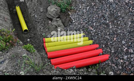 L'immagine cattura un cantiere in cui i tubi corrugati gialli e rossi luminosi sono disposti a terra accanto a una trincea. Il contrasto tra Foto Stock