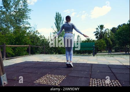 Donna attiva e in forma in un parco soleggiato, impegnata in esercizi di fitness ed equilibrio su una piattaforma sicura. Foto Stock