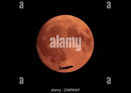Londra, Regno Unito. 18 agosto 2024. Meteo nel Regno Unito: La Sturgeon Blue Supermoon (Waxing Gibbous) al 99% vede un jet passeggeri attraversare la superficie lunare vista dal nord-ovest di Londra alle 21:11 di domenica sera. Tradizionalmente chiamato Sturgeon Moon perché lo storione gigante dei grandi Laghi e del lago Champlain erano più facilmente catturati durante questa parte dell'estate," secondo l'Almanacco dell'Old Farmer. Crediti: Guy Corbishley/Alamy Live News Foto Stock