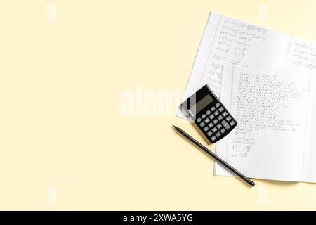 Copybook con formule matematiche scritte a mano, matita e calcolatrice su sfondo giallo Foto Stock