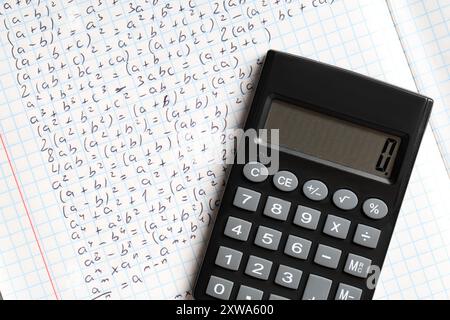 Copybook con formule matematiche scritte a mano e calcolatrice come sfondo, primo piano Foto Stock