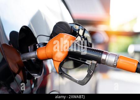 Ugello del carburante inserito nel serbatoio del carburante dell'auto mentre viene rifornito dalla pompa della stazione di servizio. Ugello della pompa del gas in una mano che rifornisce un'auto al serbatoio del gas Foto Stock