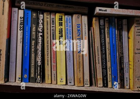 Uno scaffale di libri cartacei ben letti, di auto-aiuto e di lavoro degli anni '1970 appartenenti a vecchi genitori boomer che vivono ancora nella propria casa Foto Stock