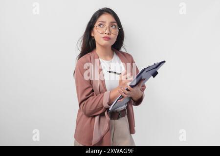 Giovane donna asiatica premurosa in occhiali da vista che tiene un documento e mette in attesa l'idea di trovare, isolata su sfondo bianco. Foto Stock