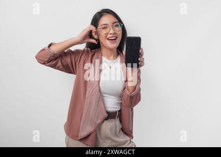 Graziosa donna d'affari asiatica in occhiali da vista che presenta uno spazio di copia sul suo schermo del telefono mentre fa la forma del cuore delle dita, isolata da sfondo bianco. Foto Stock