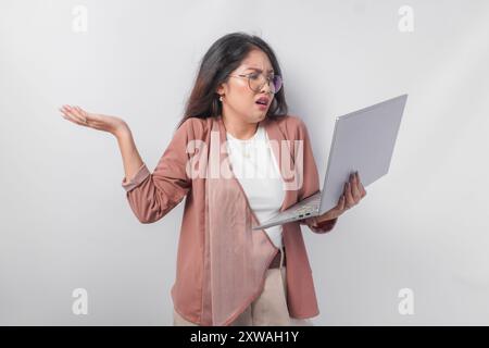 Donna asiatica confusa che tiene un notebook pensando di stressare il carico di lavoro, isolata su sfondo bianco. Foto Stock