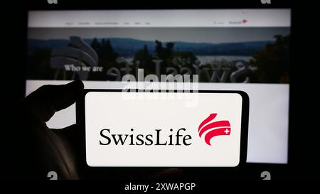 Persona che detiene un cellulare con il logo della compagnia di assicurazioni Swiss Life Holding AG davanti alla pagina web dell'azienda. Mettere a fuoco il display del telefono. Foto Stock