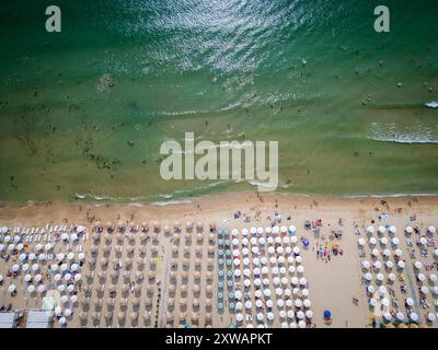 Video di una spiaggia affollata con file di ombrelloni e bagnanti, adagiati contro le dolci onde dell'oceano. La vista aerea cattura i vivaci Foto Stock