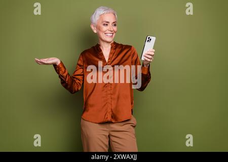 Ritratto fotografico di una bella signora pensionista foto conservare uno spazio vuoto vestito elegante in formalwear marrone isolato su sfondo color cachi Foto Stock