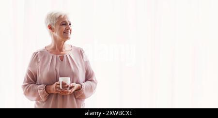 Malinconici old Lady con la tazza di stare accanto alla finestra Foto Stock