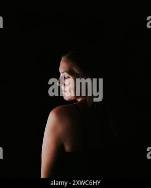 Ritratto di una donna attraente in una stanza buia che guarda sulla spalla. Foto Stock