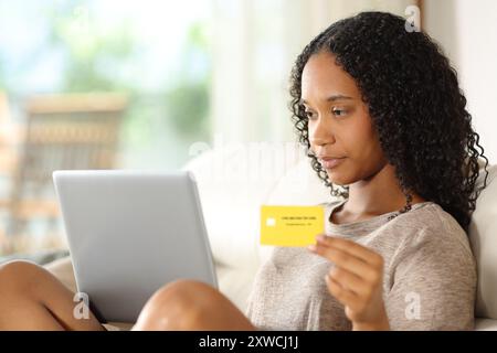 Donna nera seria che acquista online con laptop e carta di credito a casa Foto Stock