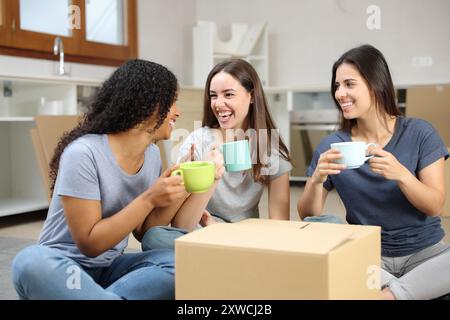 Tre compagni di stanza felici che parlano e riposano, si trasferiscono a casa in cucina Foto Stock