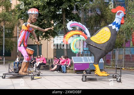 Carri allegorici, batterista in costume colorato e grande gallina o gallo colorato, la sfilata annuale del carnevale di Belfast Mela nel centro della città. Belfast, Regno Unito - 17 agosto 2024. Foto Stock