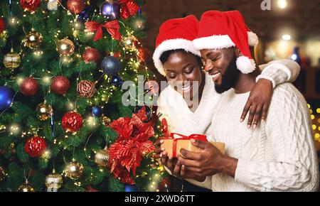 Ritratto di felice afro giovane azienda dono e di stare vicino a albero di Natale Foto Stock
