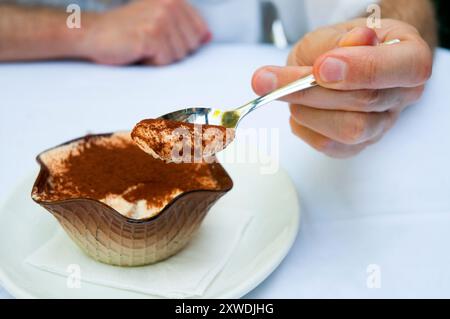 La mano dell'uomo che offre un cucchiaio di tiramisù. Vista ravvicinata. Foto Stock