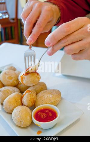 Le mani dell'uomo che si servono papas arrugadas con salsa mojo rossa in un ristorante delle Canarie. Isole Canarie, Spagna. Foto Stock