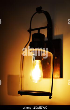 Vecchia lampada a lanterna industriale sulla parete del soggiorno. Telaio in metallo nero invecchiato con vetro intorno alla lampadina illuminata Foto Stock