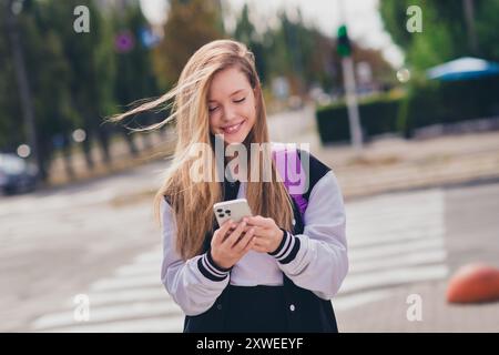 Foto ritratto di una bella ragazza adolescente che tiene il dispositivo influencer vestito elegante vestito uniforme cammina fuori sfondo verde parco Foto Stock