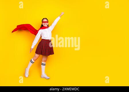 Foto a tutto corpo di una studentessa adolescente diligente supereroina volante vestita elegante e isolata su sfondo giallo Foto Stock