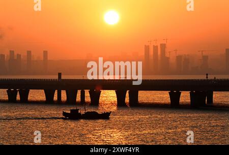 (240819) -- QINGDAO, 19 agosto 2024 (Xinhua) -- Un peschereccio si muove vicino al ponte della baia di Jiaozhou all'alba a Qingdao, nella provincia di Shandong, Cina orientale, 1 gennaio 2024. (Xinhua/li Ziheng) Foto Stock