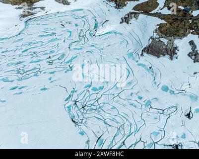 Vista aerea del lago ghiacciato Prestesteinsvatnet, la neve che scioglie crea piccole piscine blu sulla superficie ghiacciata, la montagna che attraversa Sognefjellsvegen, Sognef Foto Stock