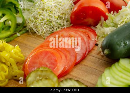 Una vista di una pila di pomodori a fette, tra le molte altre verdure su una tavola di legno. Foto Stock