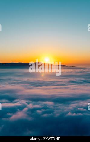 Il sole dorato sorge dietro le montagne, illuminando un mare da sogno di nuvole Foto Stock