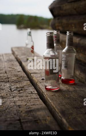 Heinola, Finlandia. 7 luglio 2024 - bottiglie vuote su una panchina di legno vicino a un lago con un tranquillo sfondo naturale Foto Stock