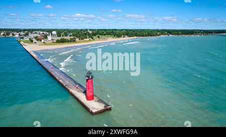 Vista aerea del faro rosso sul molo con la città costiera sullo sfondo Foto Stock