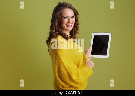 felice donna sana di mezza età su sfondo verde in maglione giallo tablet digitale schermo vuoto. Foto Stock
