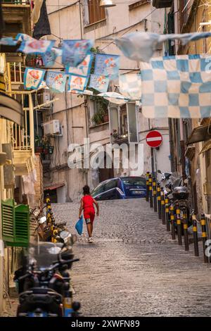 Napoli, Italia - 22 giugno 2024: Un giovane non identificato che cammina su una strada di napoli con bandiere e vestiti che si asciugano su una corda tra l'edificio Foto Stock