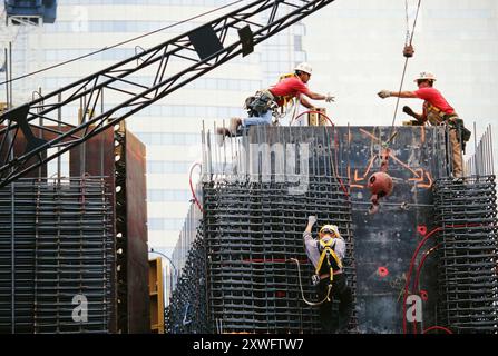 I lavoratori collaborano per sollevare i materiali durante la costruzione di una grande struttura in un cantiere urbano affollato. Foto Stock