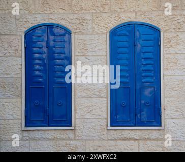 Persiane in metallo blu, che coprono finestre ad arco in un muro di pietra, tipiche degli edifici della vecchia Gerusalemme, Israele. Foto Stock