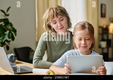 La giovane mamma moderna si diverte a stare con sua figlia, guardano cartoni animati Foto Stock