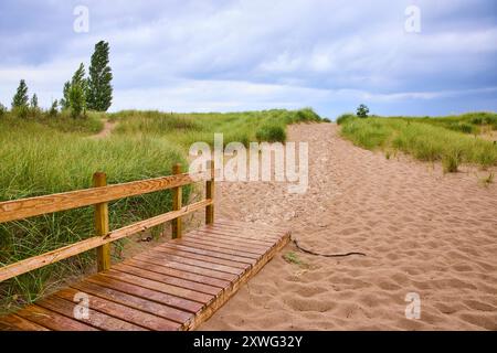 Passerella pedonale in legno sul sentiero sabbioso attraverso le dune costiere nel tardo pomeriggio Foto Stock